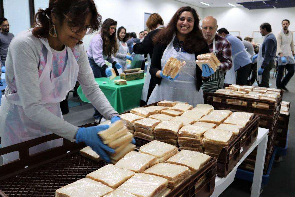 A crowded room of people make and stack hundreds of sandwiches