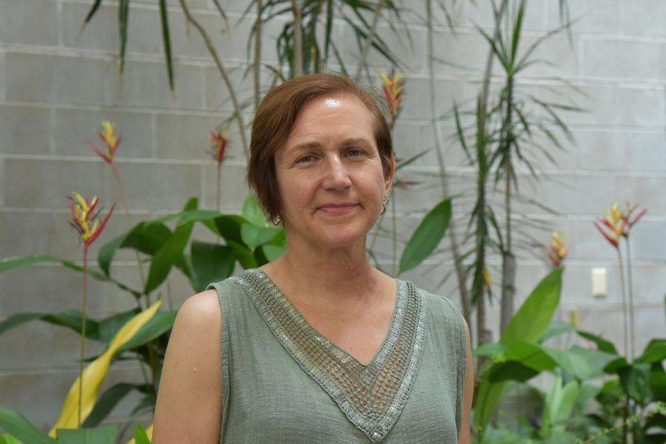 Fulbright Scholar Professor Lynn Cazabon stands smiling at the camera in front of lush tropical plants