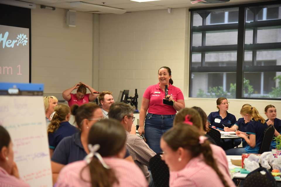 Dr Jaime Manning stands holding a microphone, speaking to a room full of students