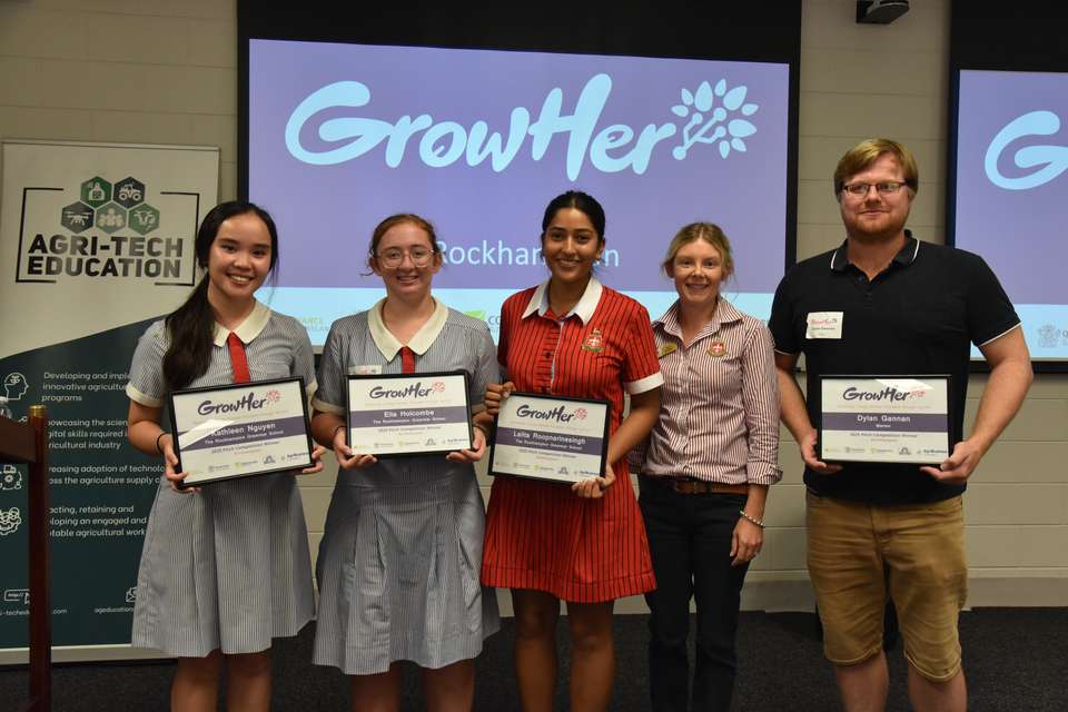 A group of five people stand together holding GrowHer event certificates, against a digital backdrop with the GrowHer logo, and a pull up banner for Agri-Tech Education