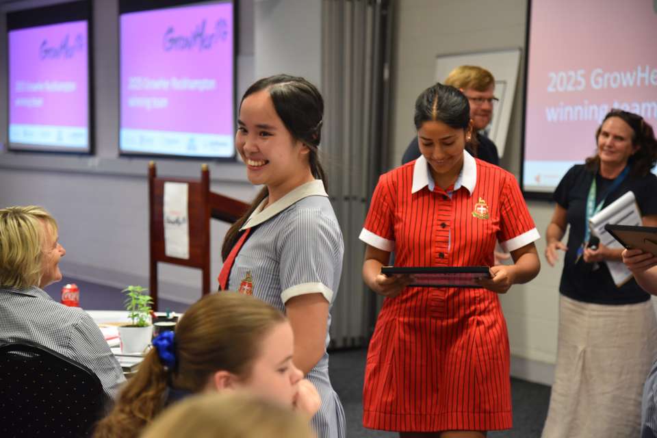 Rockhampton Grammar School student Kathleen Nguyen stands in focus, smiling after receiving her winning GrowHer event certificate; her teammate walks behind her smiling as she views her certificate in her hands