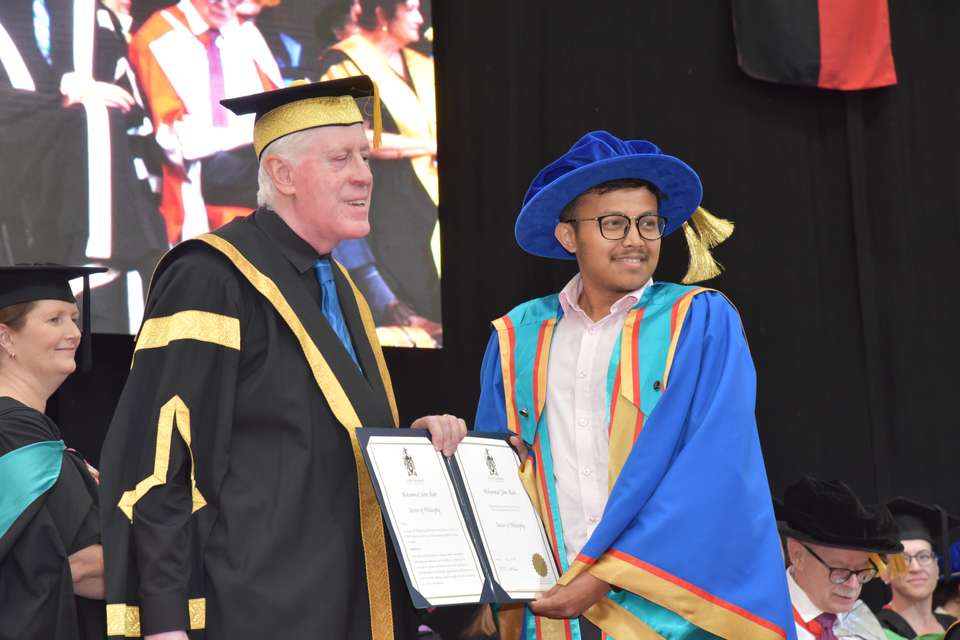 PhD graduate Jaber Alam receives his testamur from CQU Chancellor Graeme Innes AM onstage at a ceremony in Rockhampton.
