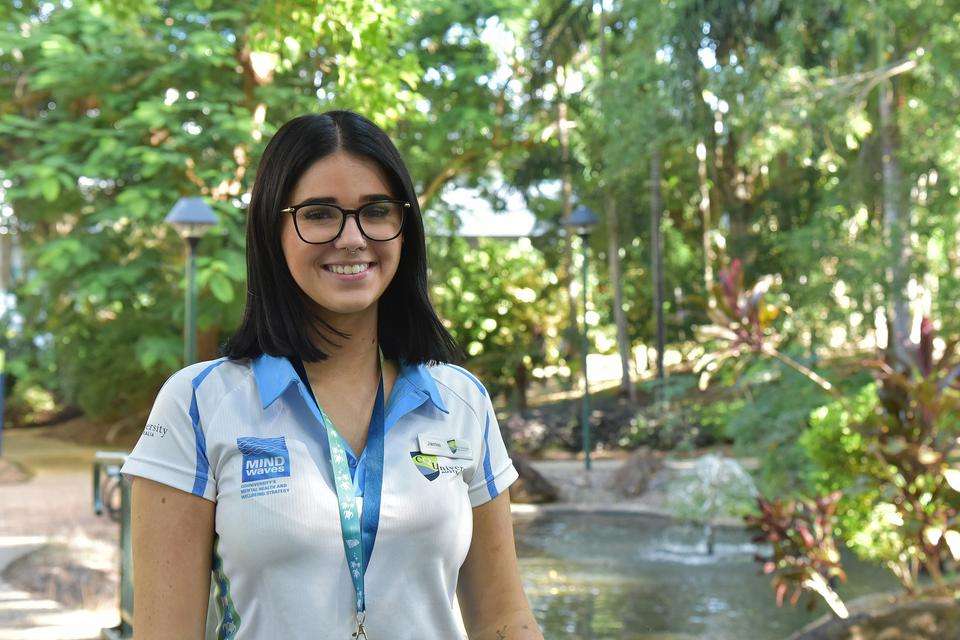 Image of a young Indigenous woman smiling at the camera with a waterfall backdrop