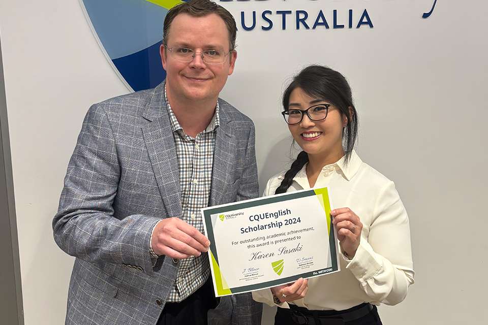 Image of a man presenting a woman with a certificate standing in front of a sign which reads CQUniversity Australia