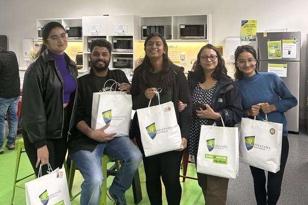 Five students hold their Campus Kindness food packs, in white paper bags with CQU logo.