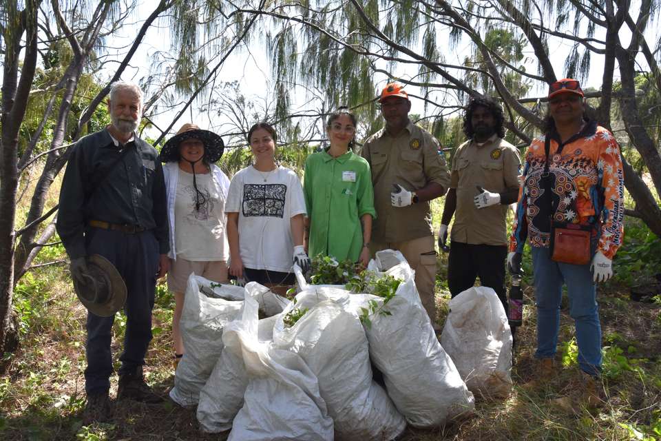 A group of conservation volunteers stand together smiling for a photo, pictured with bags of weeds they have removed from the native bushland surrounding them