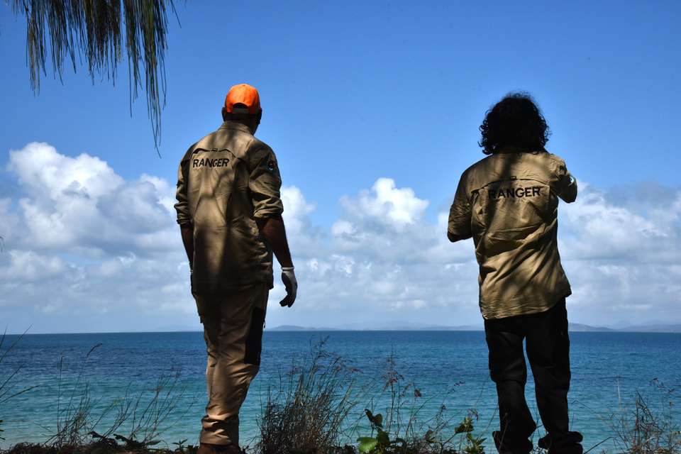 Two rangers stand atop a sand dune looking out across a blue ocean
