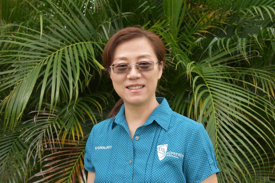 Clinical Psychology Registrar Yingying Tang dressed in a CQUniversity shirt in front of a palm tree.jpg