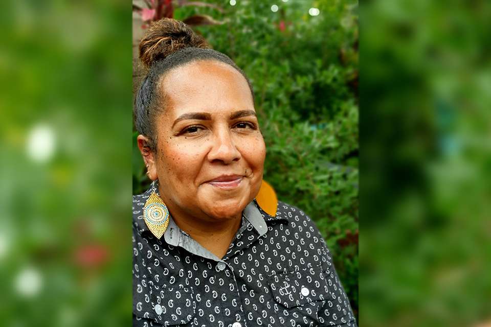 A headshot of Dr Melinda Mann, standing outside with greenery in the background