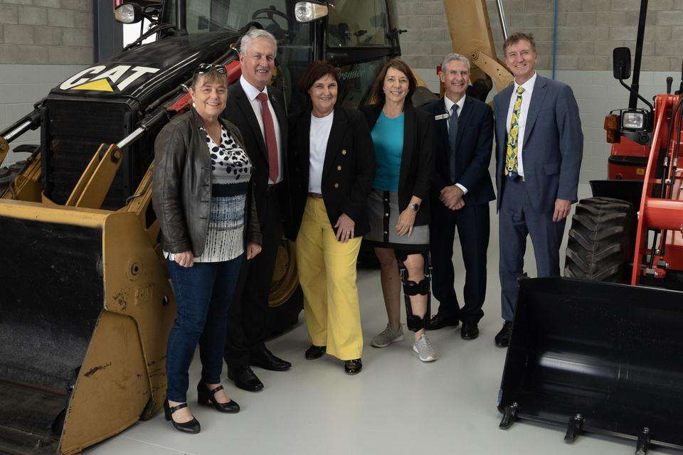 L-R: Mackay Councillor Alison Jones, Mayor Greg Williamson, Member for Mackay Julieanne Gilbert MP, Mackay Debuty Mayor Belinda Hassan, CQU Mackay AVP Professor Rob Brown and VC Professor Nick Klomp. The group stands in the new heavy auto training facility with a bulldozer in the background.