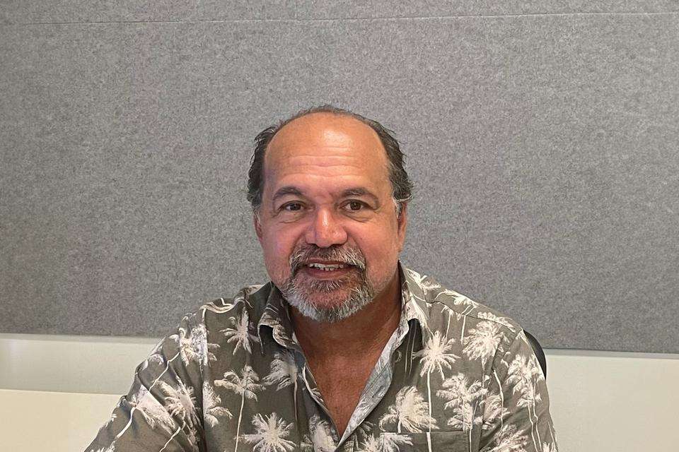 First Nations academic Dr Gary Fry sits smiling at the camera, against a grey backdrop