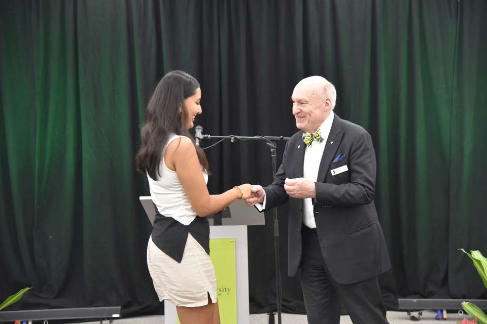 A female medical student is shaking hand with a man with a bow tie in front of a black curtain with green lighting.JPG