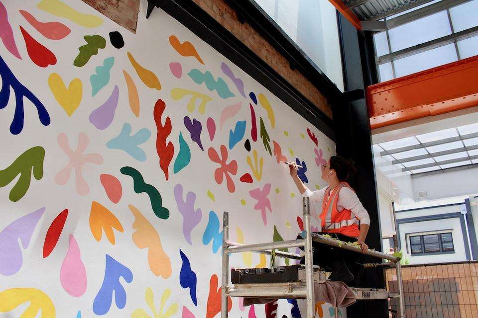 Visual artist Katie Whyte stands on scaffolding as she paints a wall mural in a public space