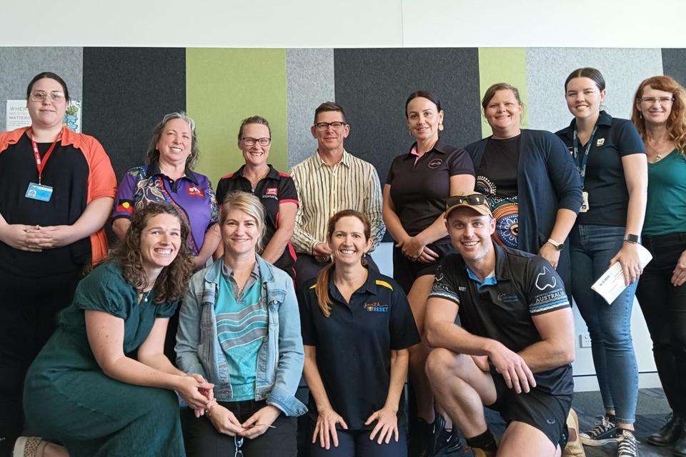 A group of 12 people pose and smile in a workshop room.