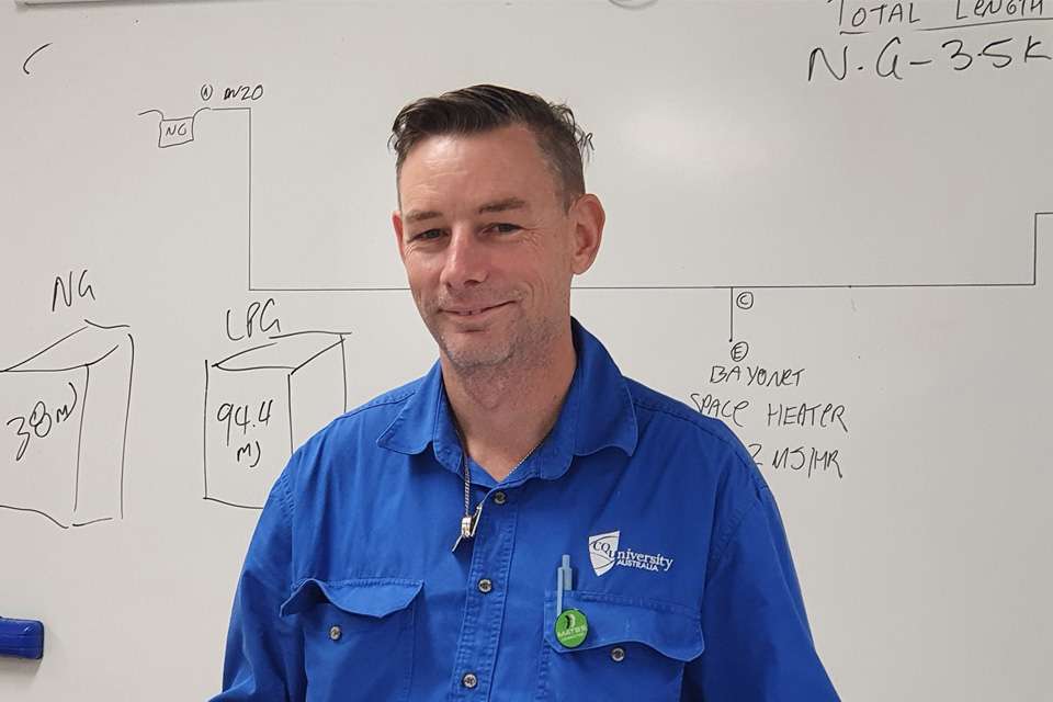 Smiling man in blue shirt stands in front of whiteboard
