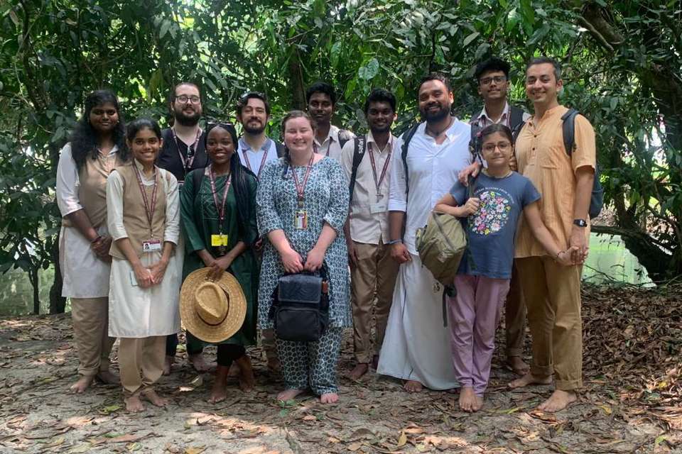 Image of a group of adults and children standing in a forest type setting in rural India