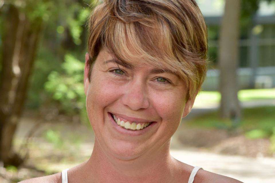 Woman wearing white singlet, with pixie cut hair looking at camera with broad smile showing teeth