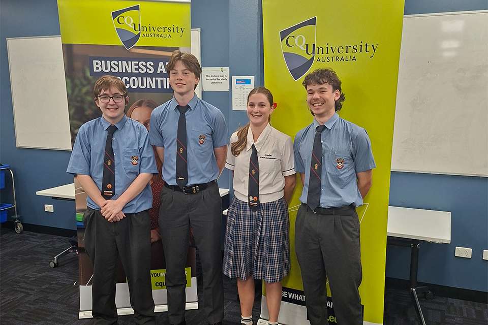 Four Shalom College students standing in front of green CQU banner