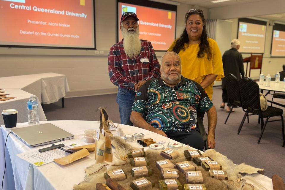 Uncle Steve Kemp sits centre, while Uncle Milton Lawton and Melanie Kemp stand, in front of a table of Yarbun Creations products.