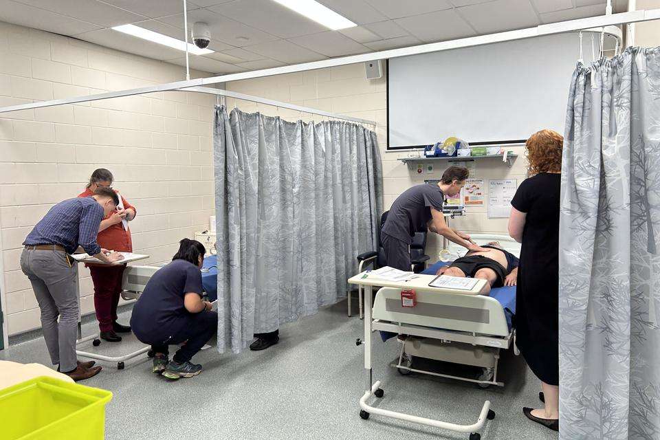 Medical and nursing students as well as supervisors attend to actors who are impersonating patients in a simulated hospital environment.