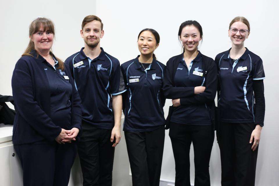 A line of five students wearing navy CQU Sonography shirts smile for camera.