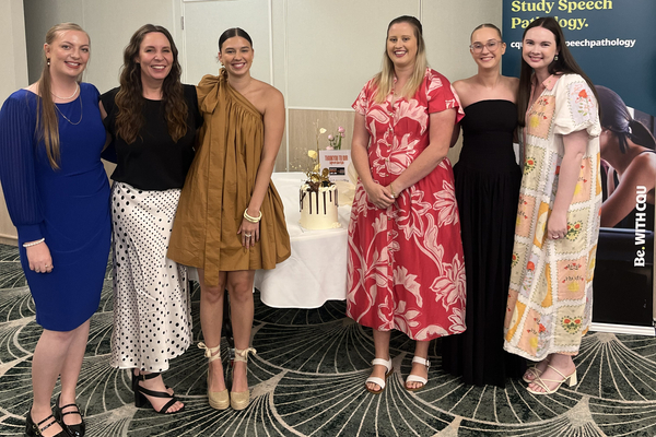 Image of six women standing near a table with a cake