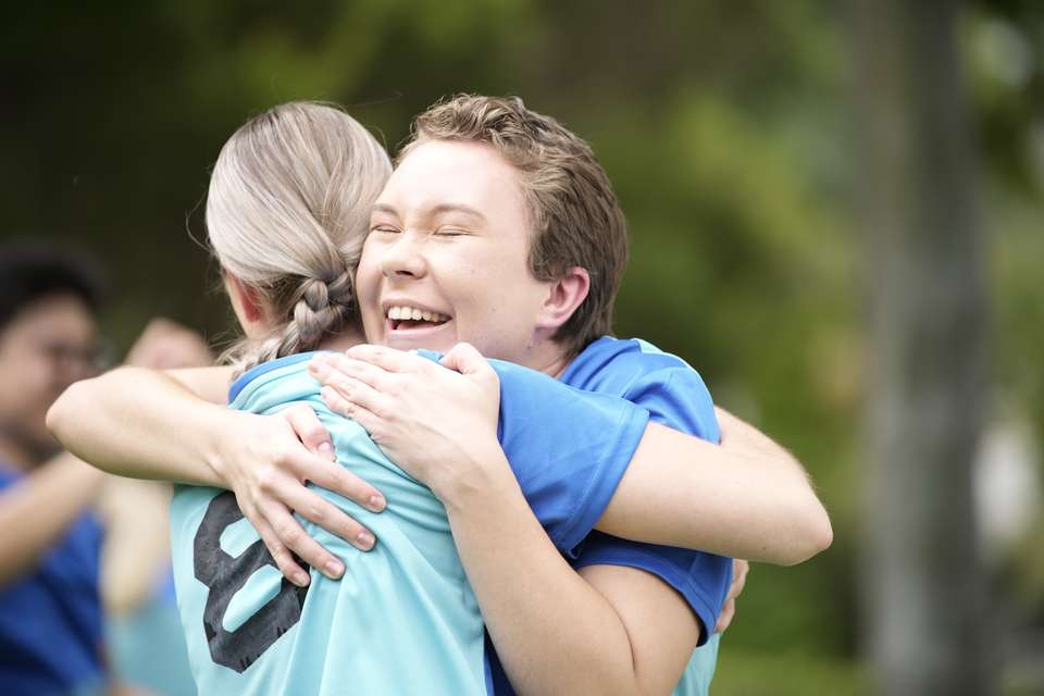 Two female soccer players wearing blue shirts celebrate on the field.