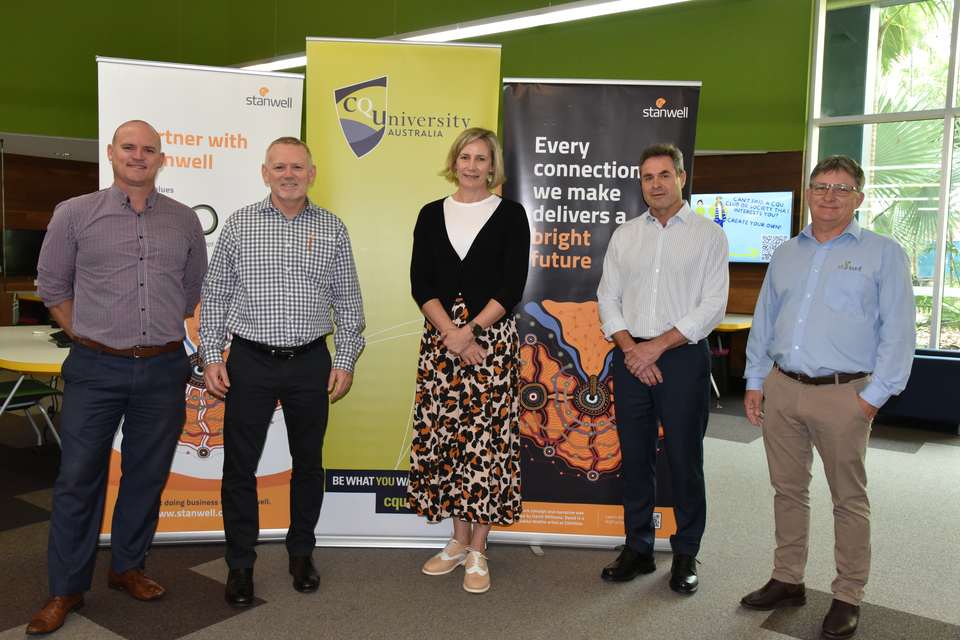 Five people stand in front of CQU and Stanwell promotional banners. There are two men on either side of a woman standing in the middle.