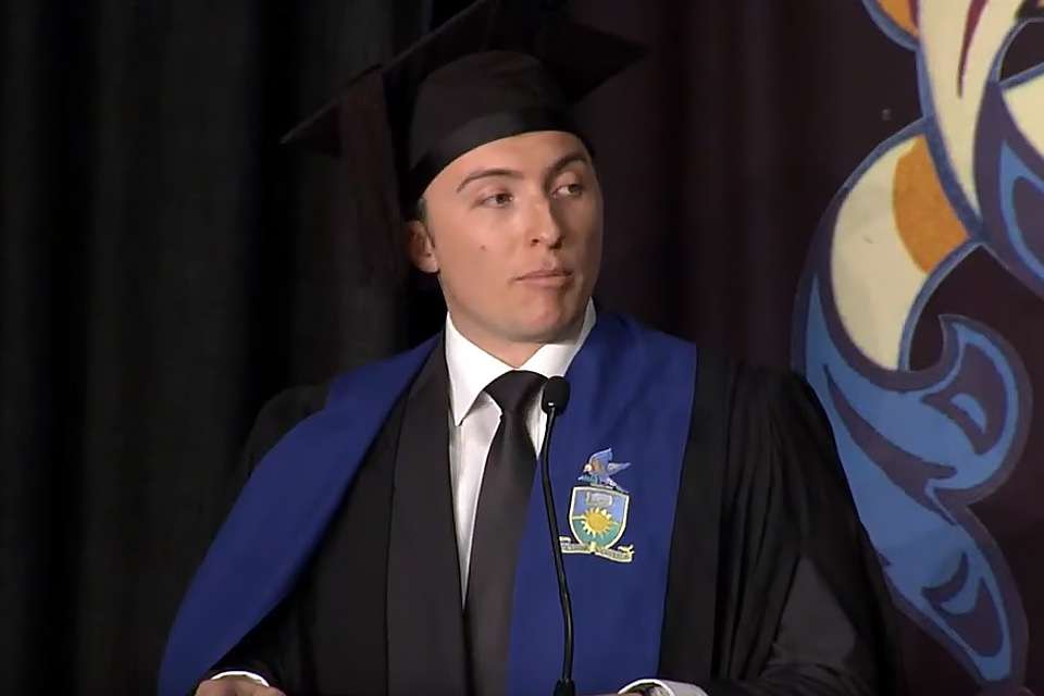 A photo of a man in graduation gown and cap standing at a podium