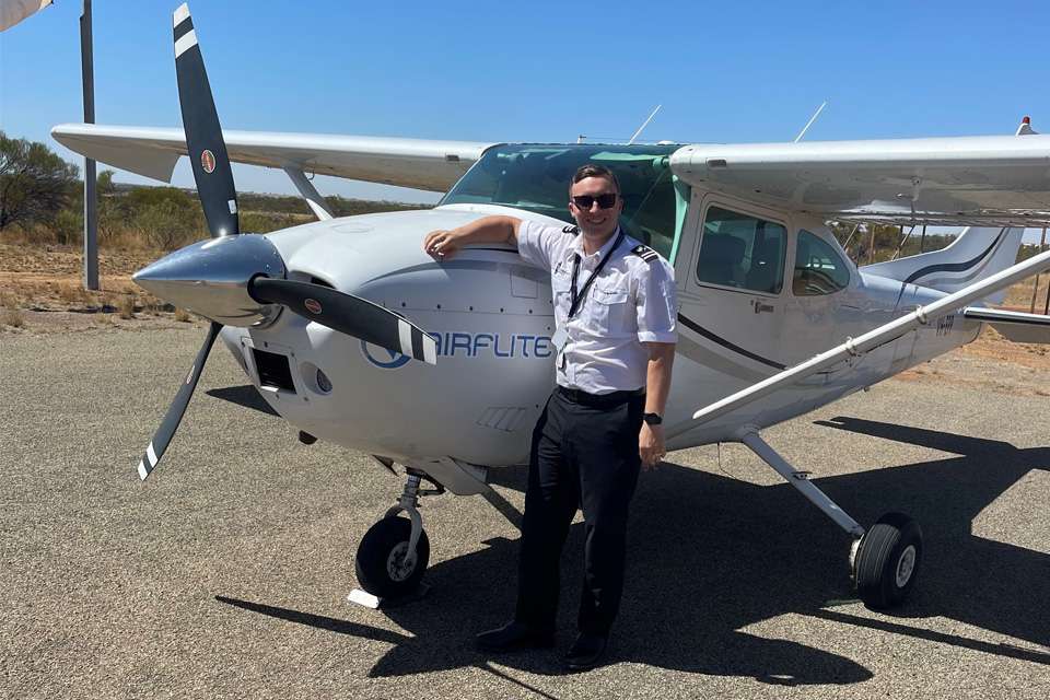 A photo of a man dressed in pilot attire standing in front of a light airplane