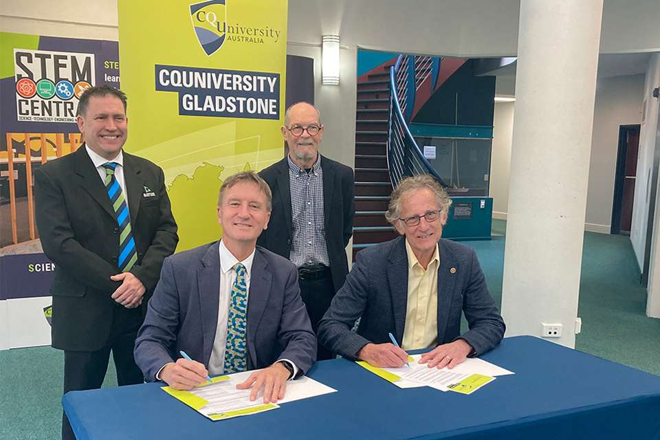 Stakeholders from CQU, Gladstone Council and Sunshine Hydro signing paperwork and smilling for photo. CQUniversity Gladstone and STEM Central banners are in the background