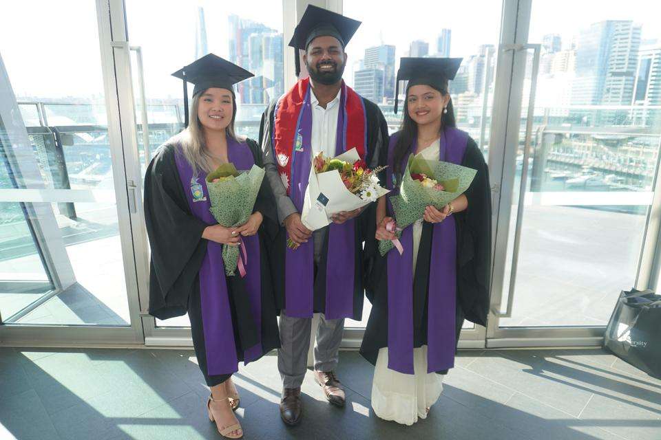 Students standing in regalia holding flowers