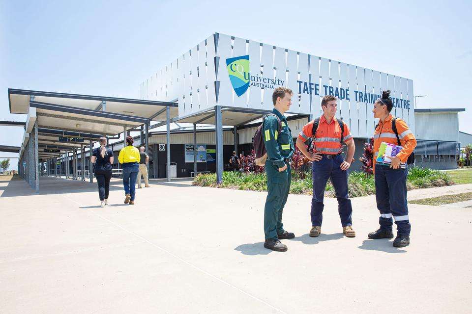 Three young people in high-vis clothing stand and talk to each other on a path outside the CQU Mackay Ooralea campus TAFE Trades Training Centre