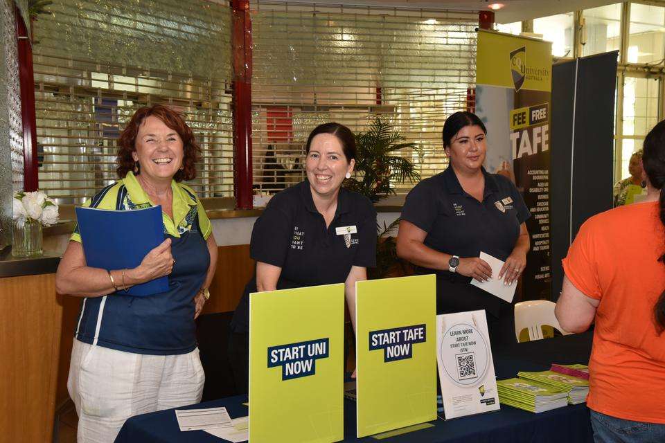 CQU staff members at a stall promoting programs for school students, stand smiling at the camera