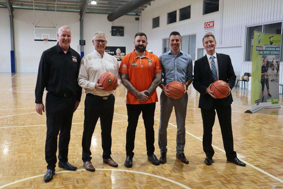 Five men, some holding basketballs, on a court smiling at the camera