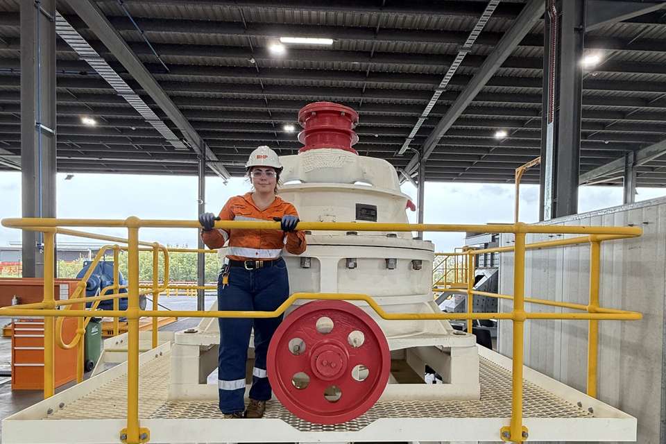 Young woman in high visibility clothing and hardhat standing in a large industrial style workshed