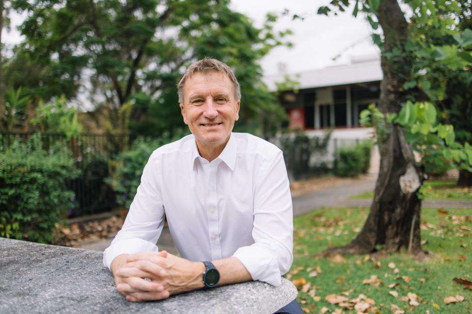 Vice-Chancellor and President Professor Nick Klomp wearing a long sleeved white business shirt, sitting at a table in an outdoor park area looking at the camera and smiling