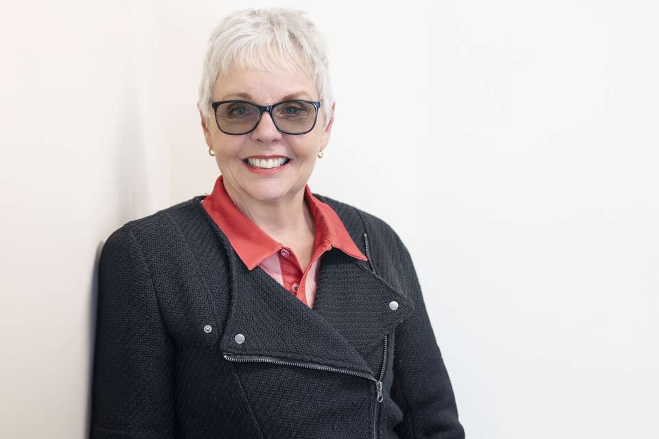 Dr Vicki Pascoe stands next to a white wall.