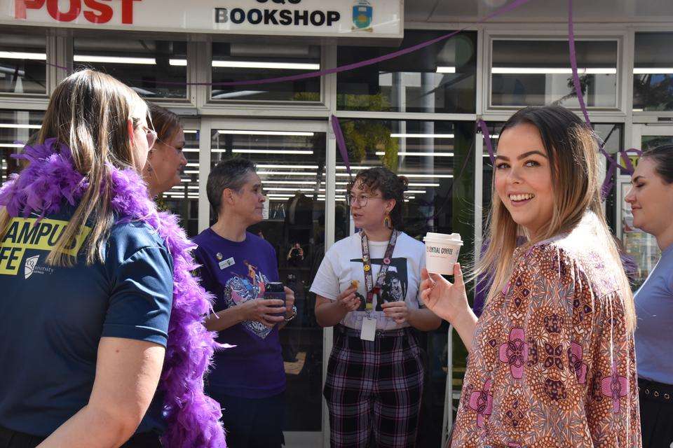 CQU staff gather together to celebrate Wear It Purple Day; they are chatting with each other over morning tea, while CQU staff member Gabrielle Jeffs turns to smile at the camera with a coffee in hand