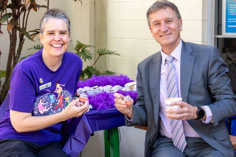 Dr Gemma Mann and Professor Nick Klomp smile and hold purple cupcakes; Nick Klomp also has a coffee in hand.