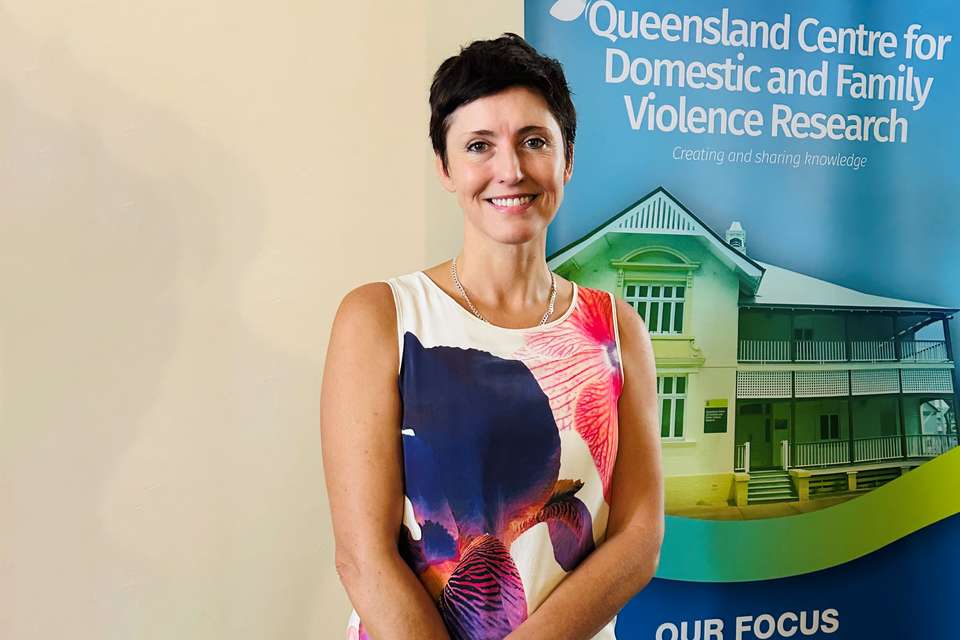 Xanthe Mallett wears a colourful short sleeve dress in front of Qld Centre for Domestic and Family Violence Research banner.jpg