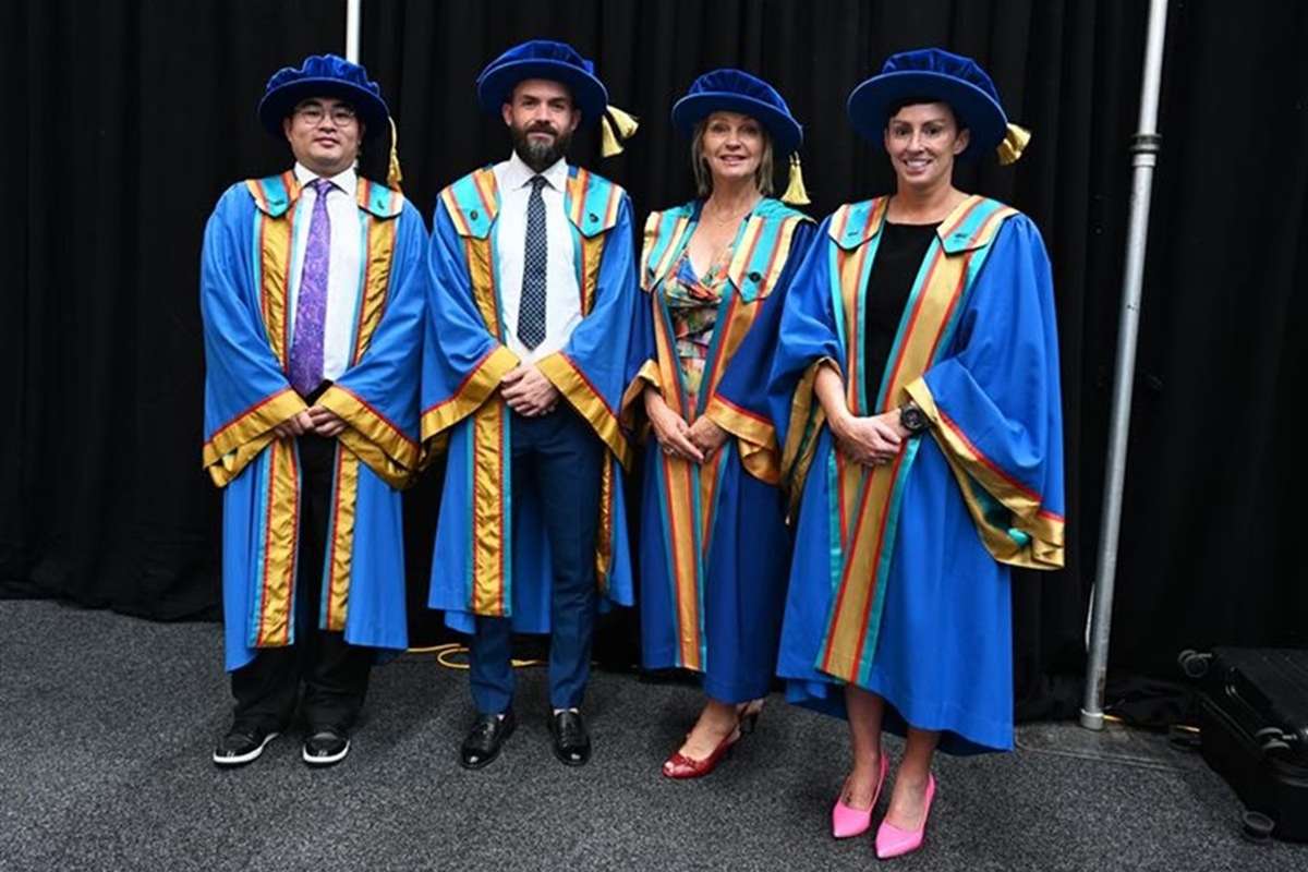 Four people in a line wearing regalia