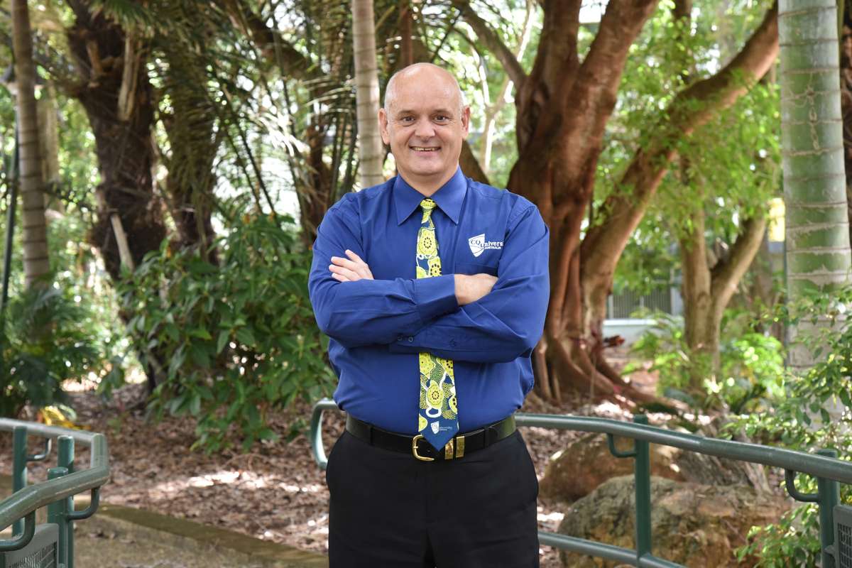Man in a blue shirt and green tie standing with his arms folded