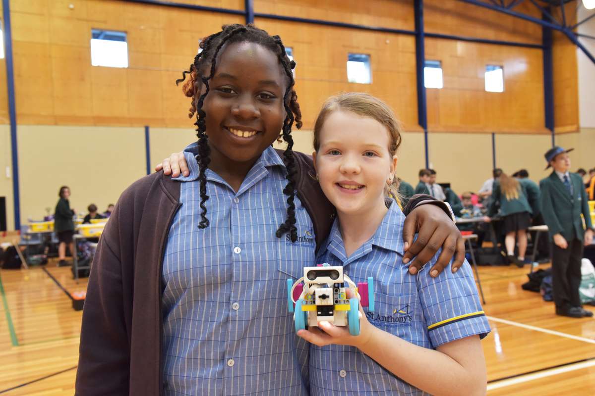 Two primary school age students in blue uniforms with a robot