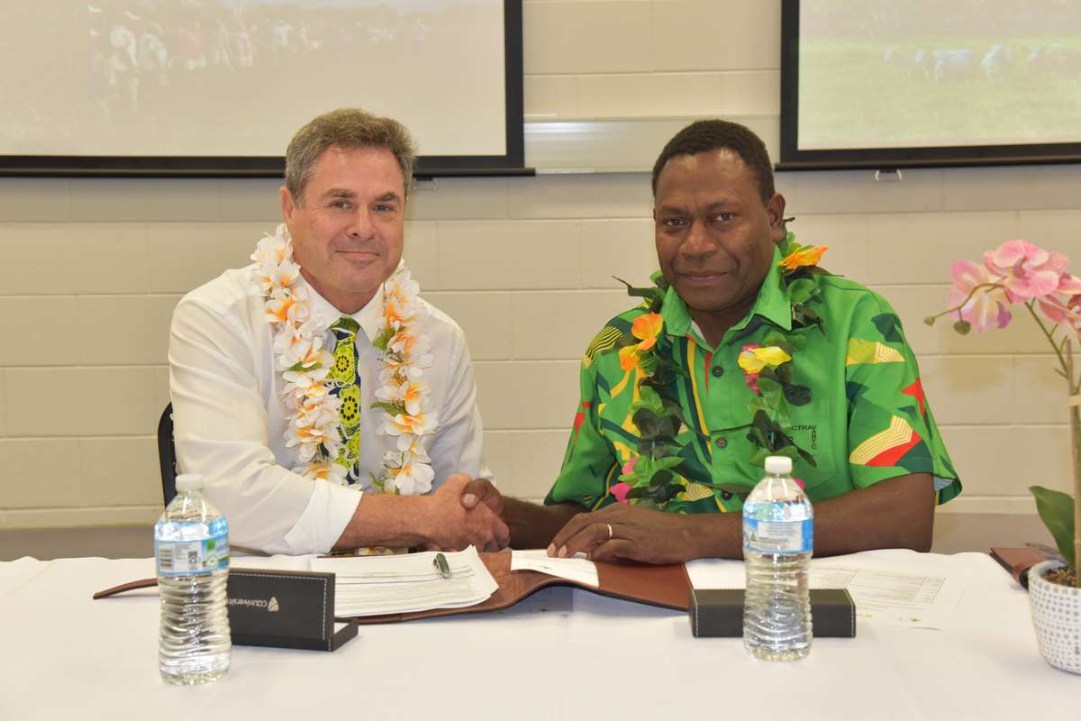 Man in white business shirt shaking hand of man in green shirt in front of paperwork