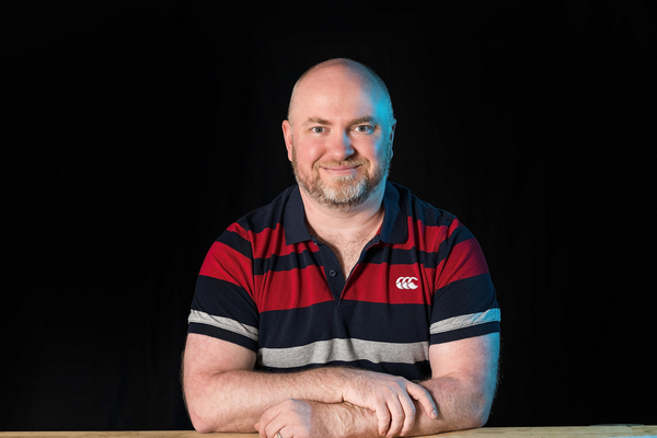 Dr Alex Russell sits at a table in front of a black backdrop.