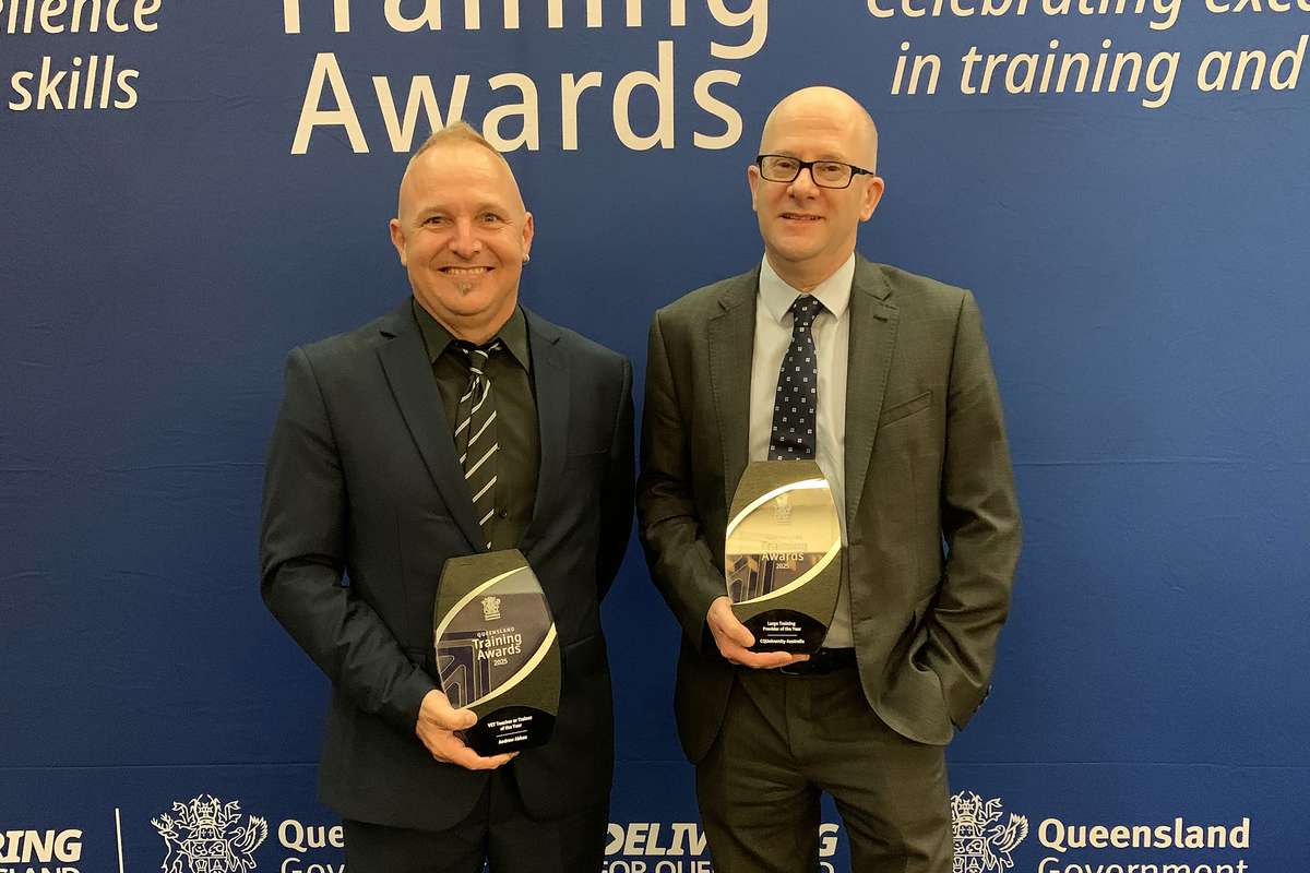 Image of two men standing in front of queensland training awards banner holding trophies