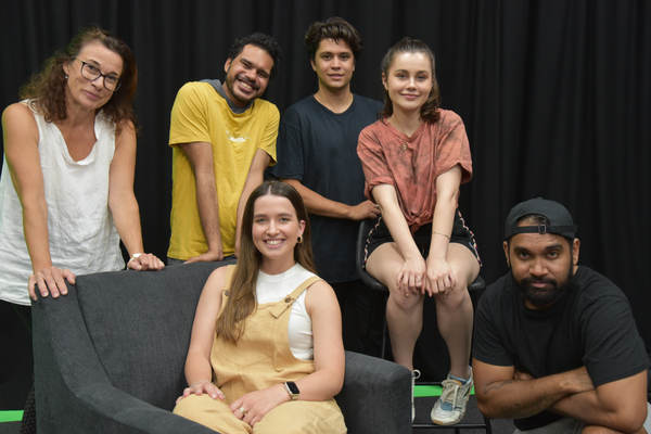 No Dramas students and researcher Linda Lorenza sitting and standing around chairs with a black curtain backdrop
