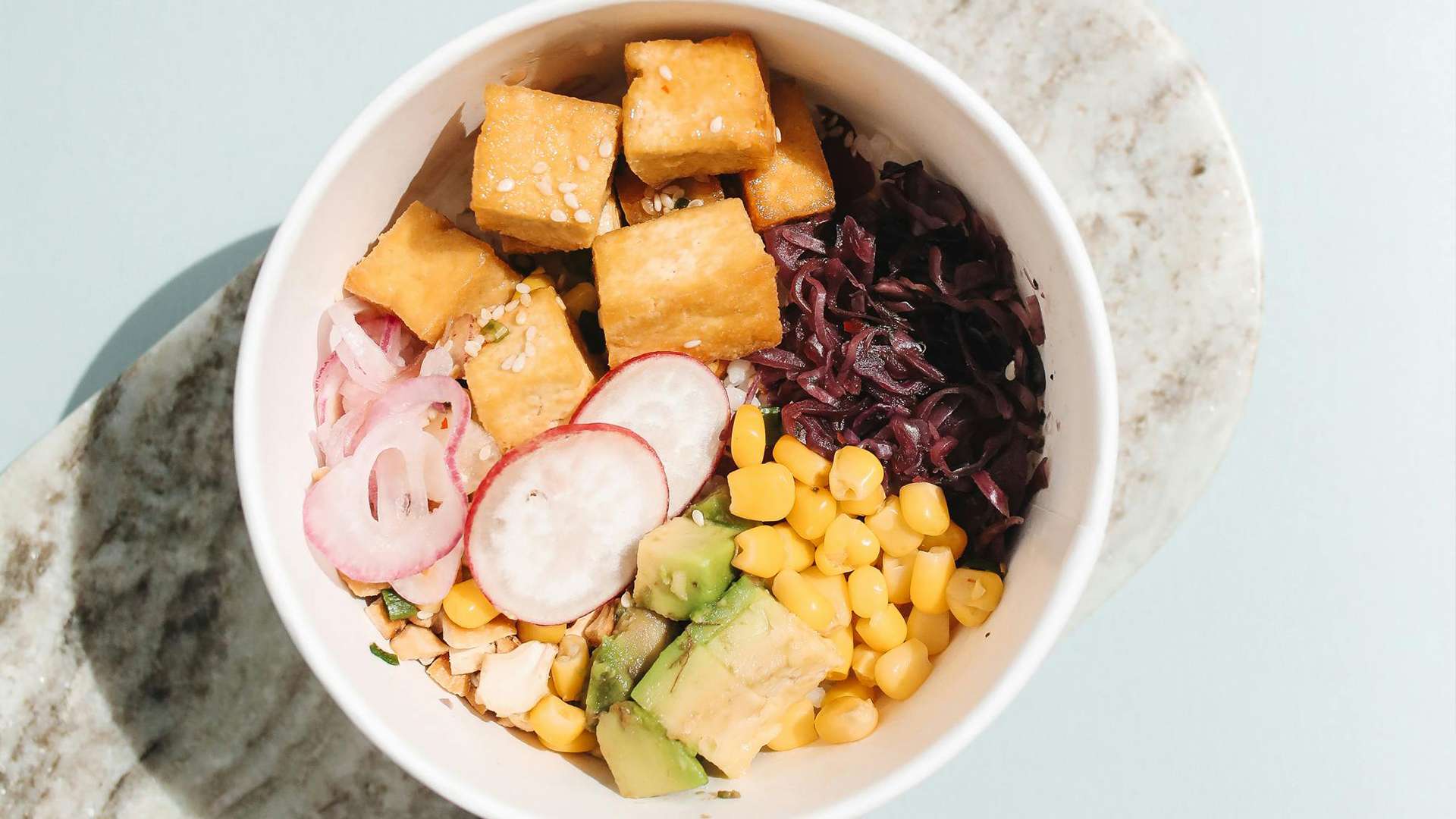 A poke bowl with tofu, radish, corn, avocado and other condiments
