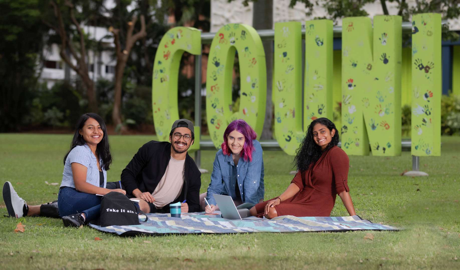 Smiling CQU male and female students sitting on grass at Rockhampton Campus.